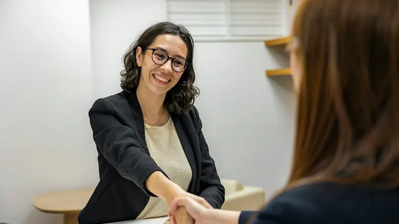 Two people greeting each other across a desk at an interview